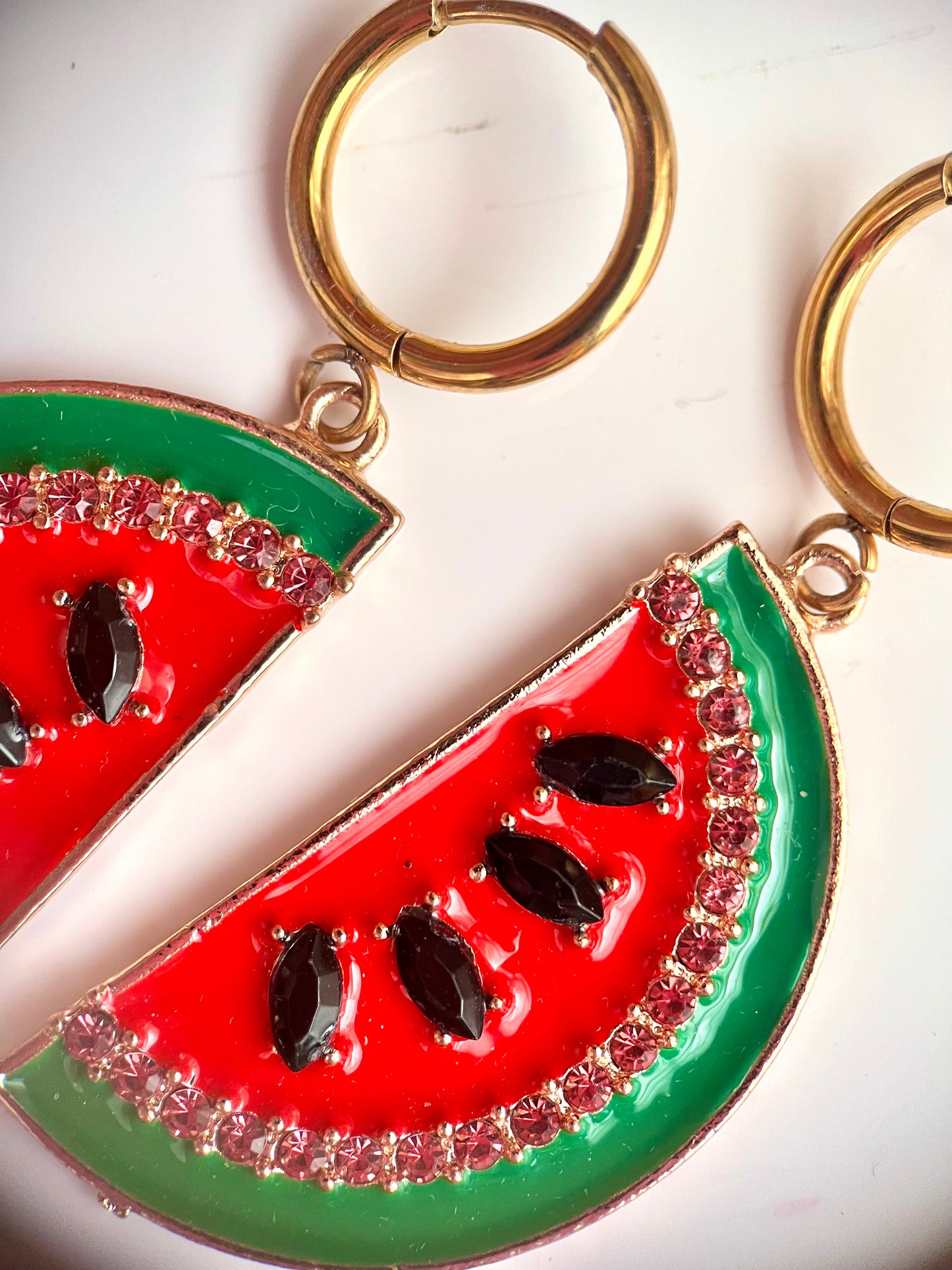 a product photo image taken from above of a pair of earrings that resemble a slice of watermelon, with a green rind and feature black rhinestones as seeds