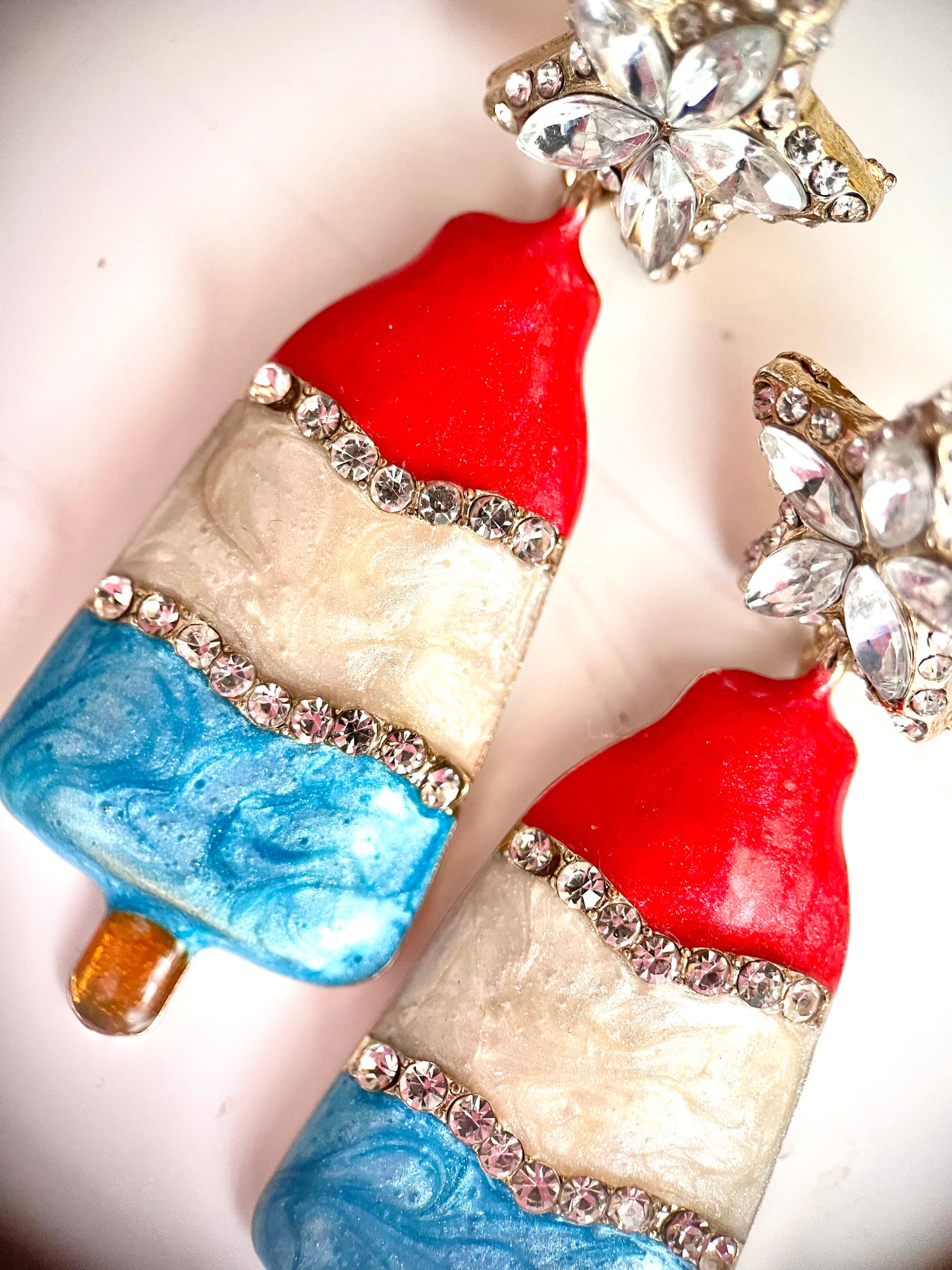 a product photo image of a pair of earrings that mimic bomb pop popsicles taken from above, featuring red white and blue fourth of july nostalgic treat